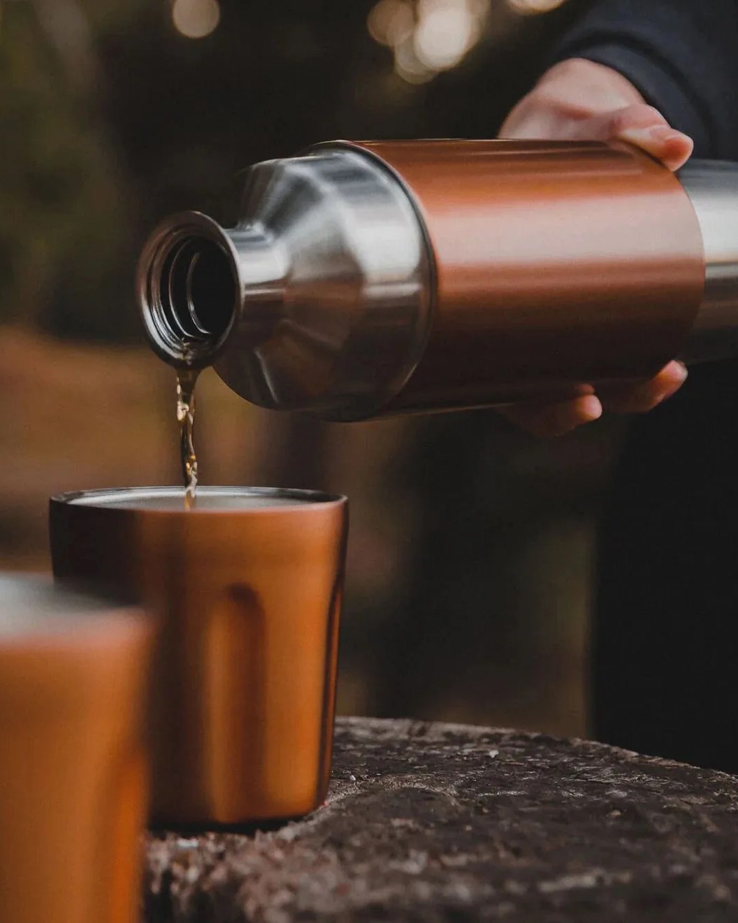 a person pouring a liquid into a glass from a high camp firelight flask 750
