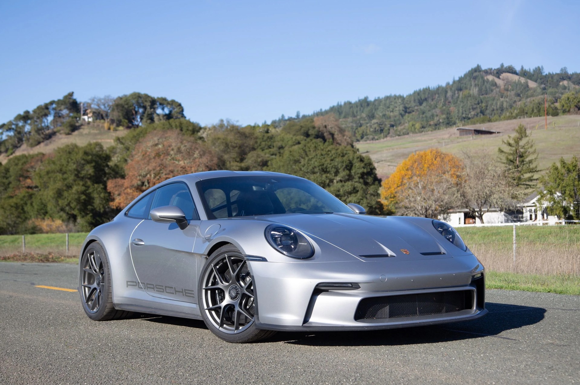 a silver sports car parked on a road with trees and hills in the background