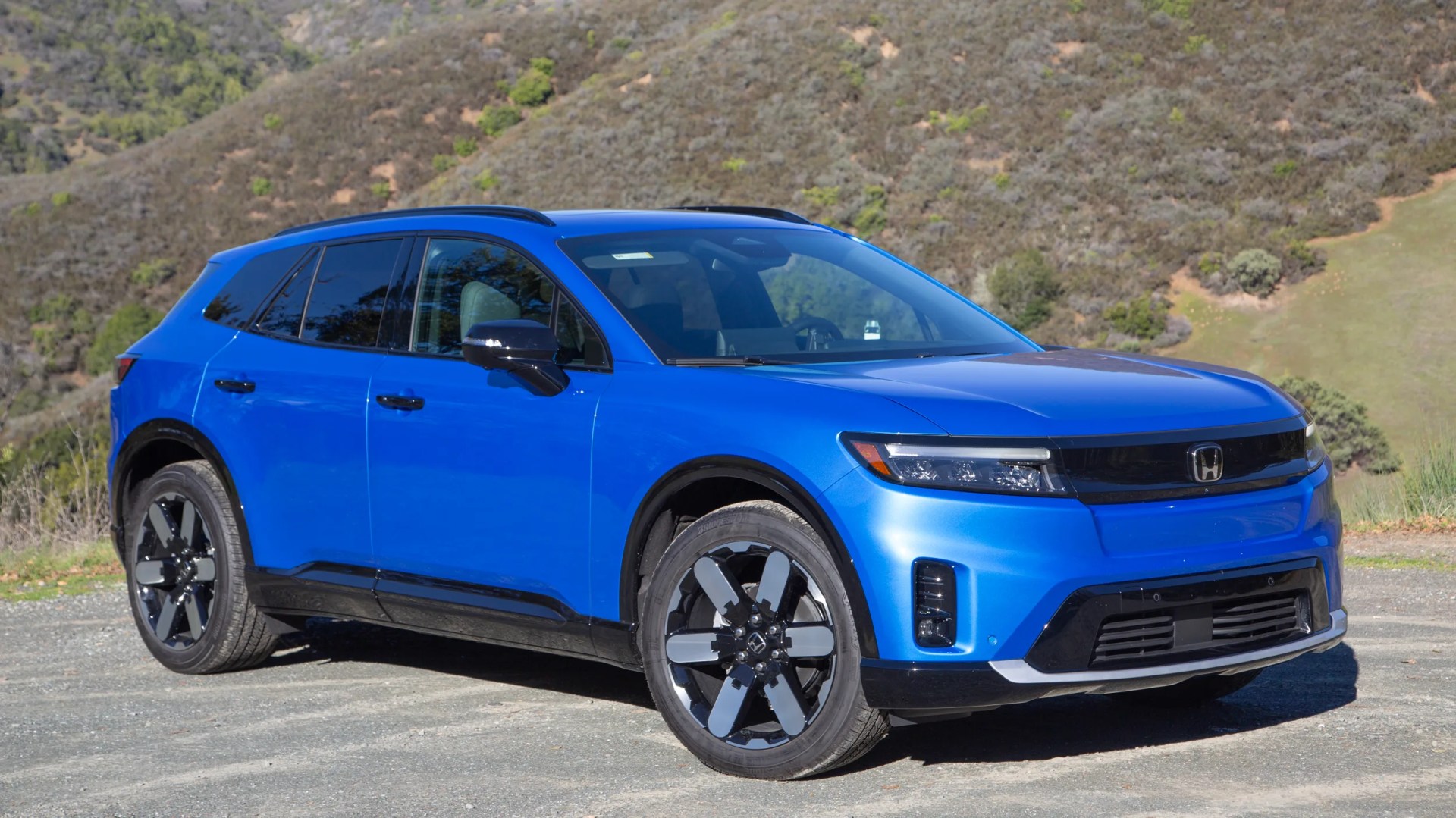 the front three quarter view of a blue 2024 honda prologue in front of a green hill