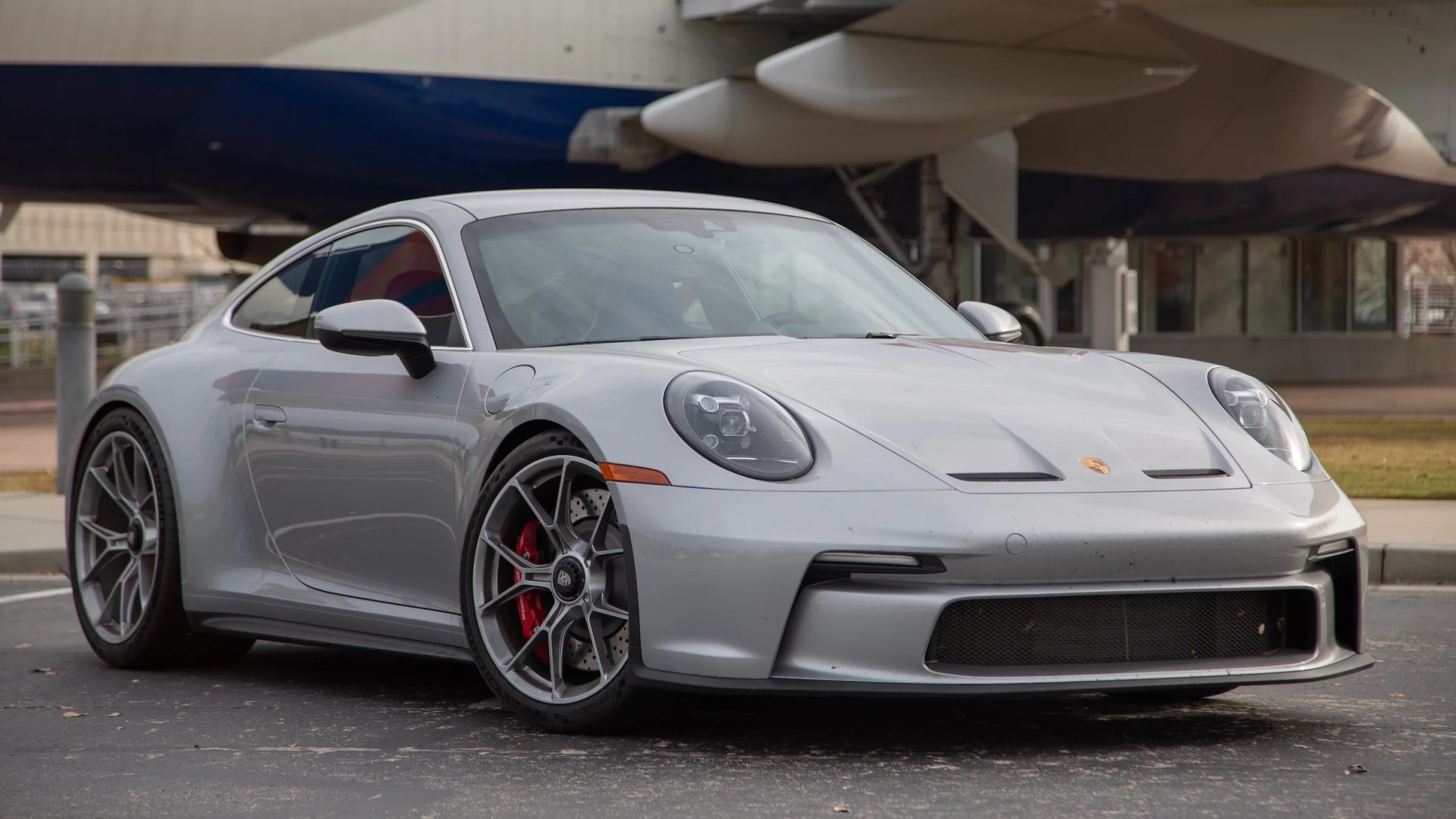 silver porsche 911 gt3 touring in front of a delta 747