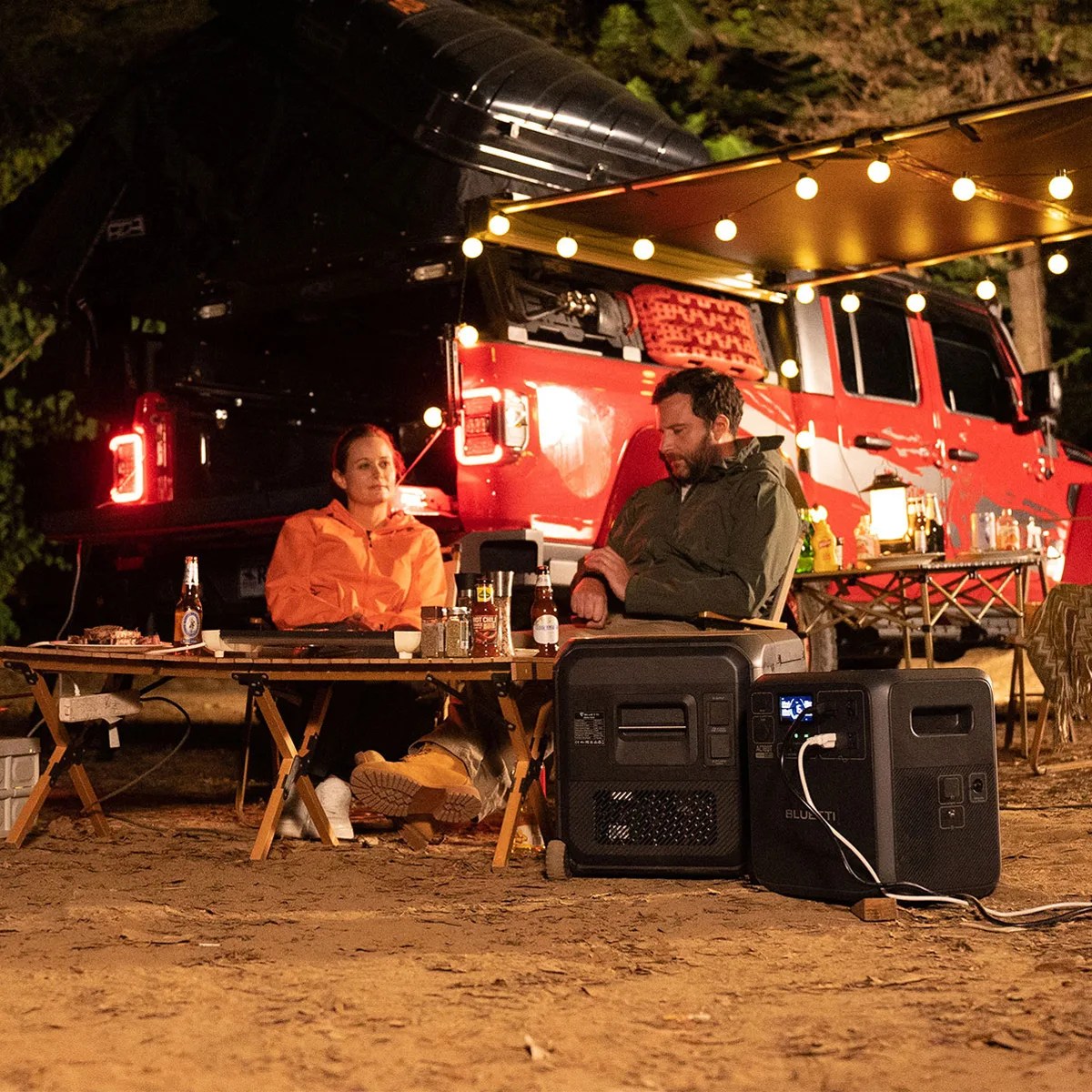 woman and man camping by trailer with fairy lights using Bluetti AC180T + Multicooler