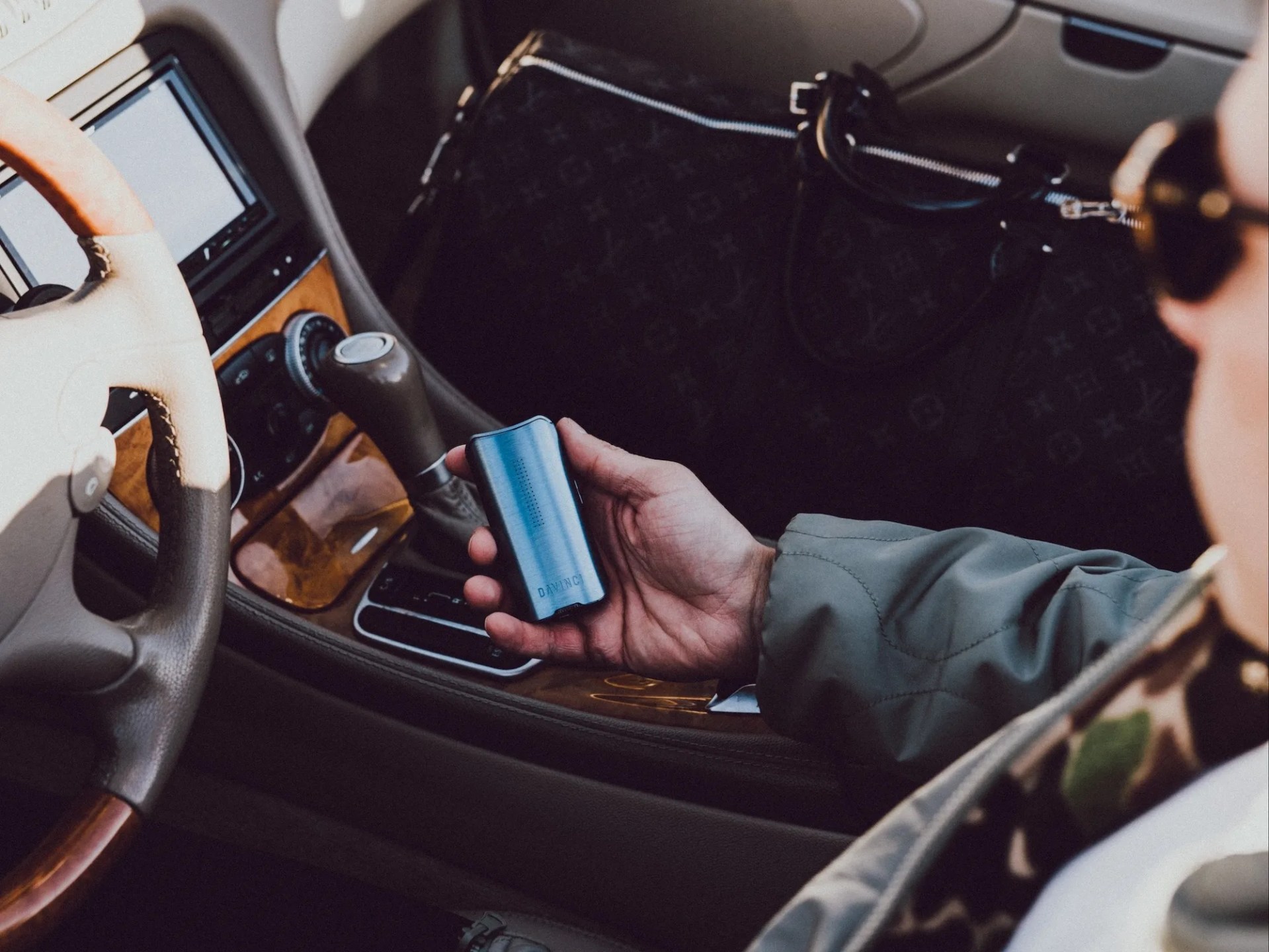A person sitting in a luxury automobile holding a Davinci vaporizer.