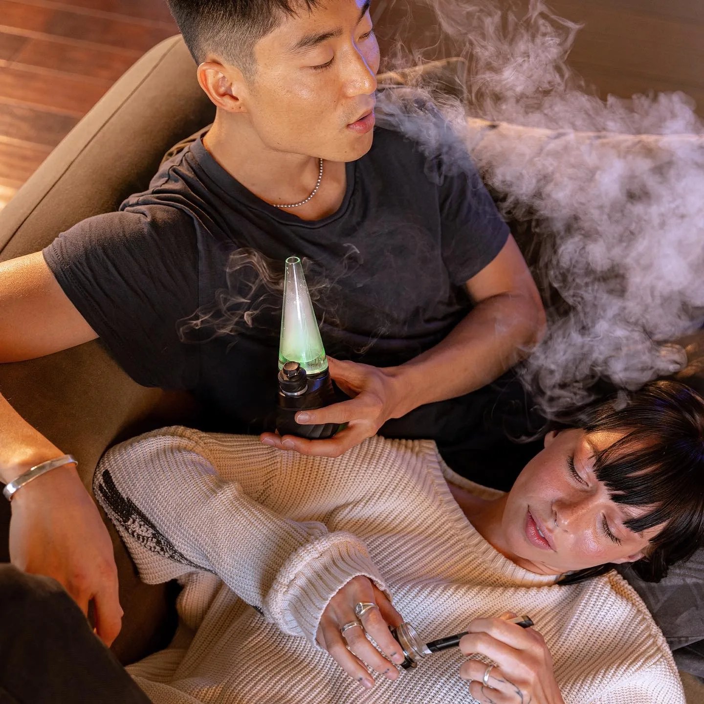 Two people laying on a couch smoking from a Puffco vaporizer