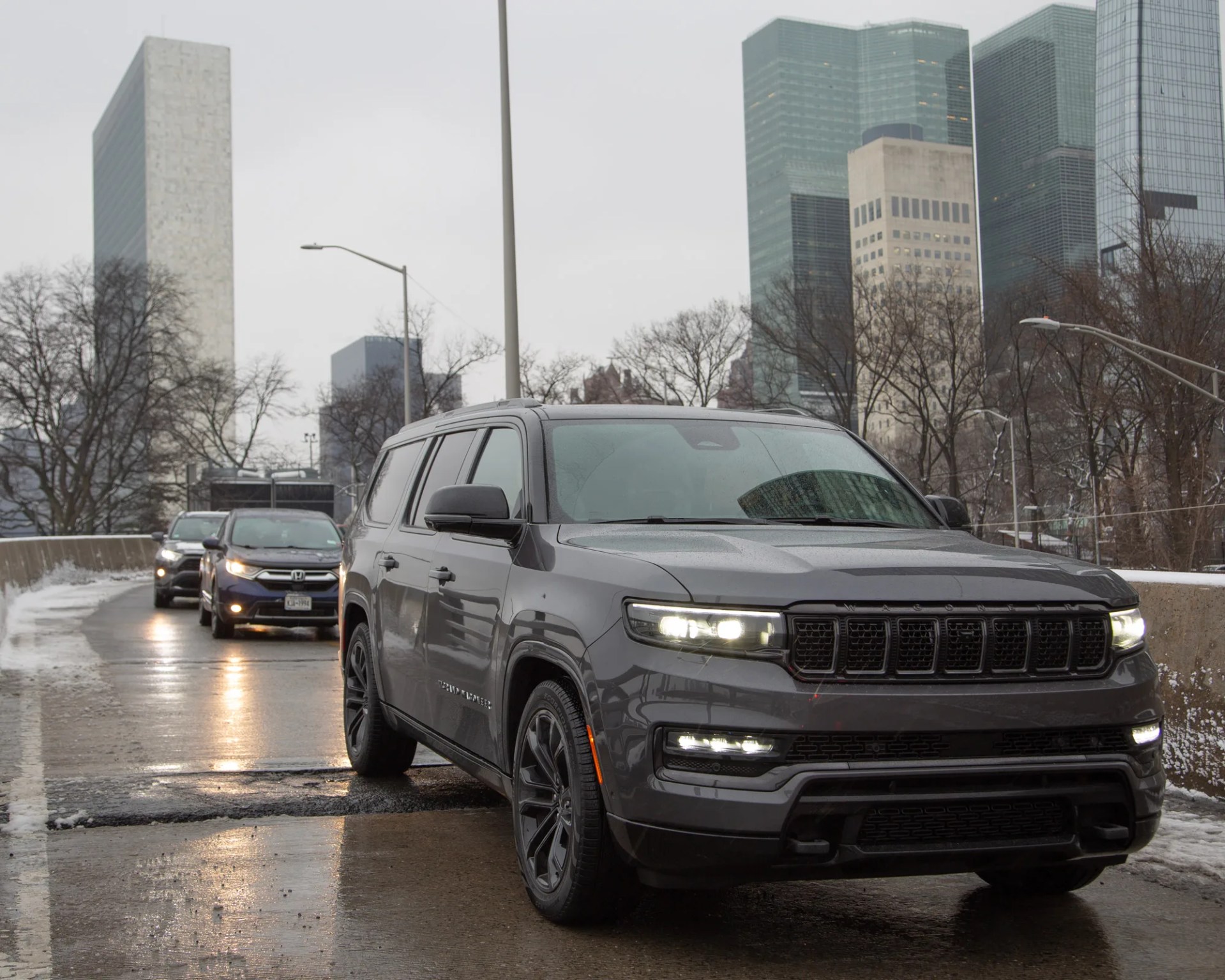gray 2024 jeep grand wagoneer L seen from the front on a city street with tall buildings in the background