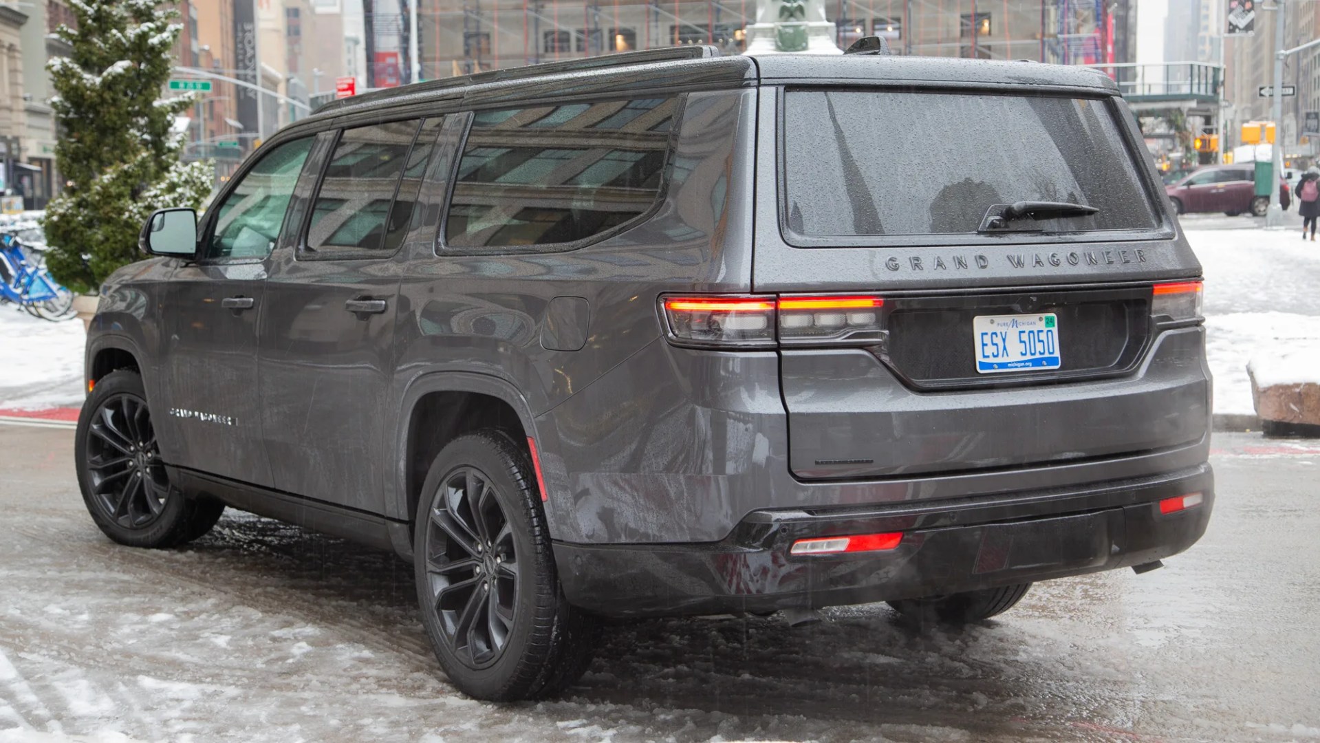 gray 2024 jeep grand wagoneer L seen from the rear on a city street in winter with tall buildings in the background