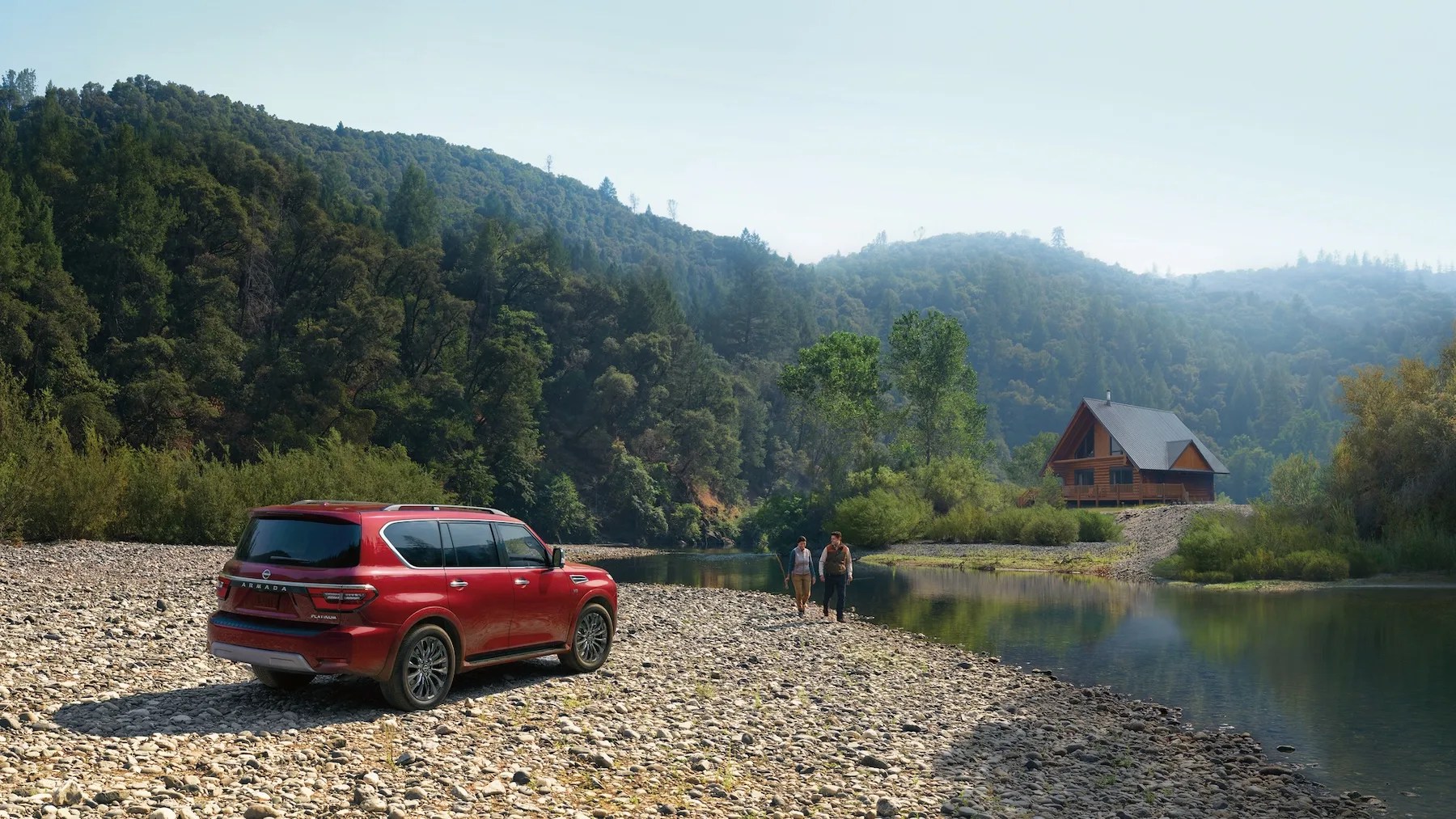 2024 nissan armada parked on a river bank with an a frame cabin in the back ground and two anglers walking along the shore