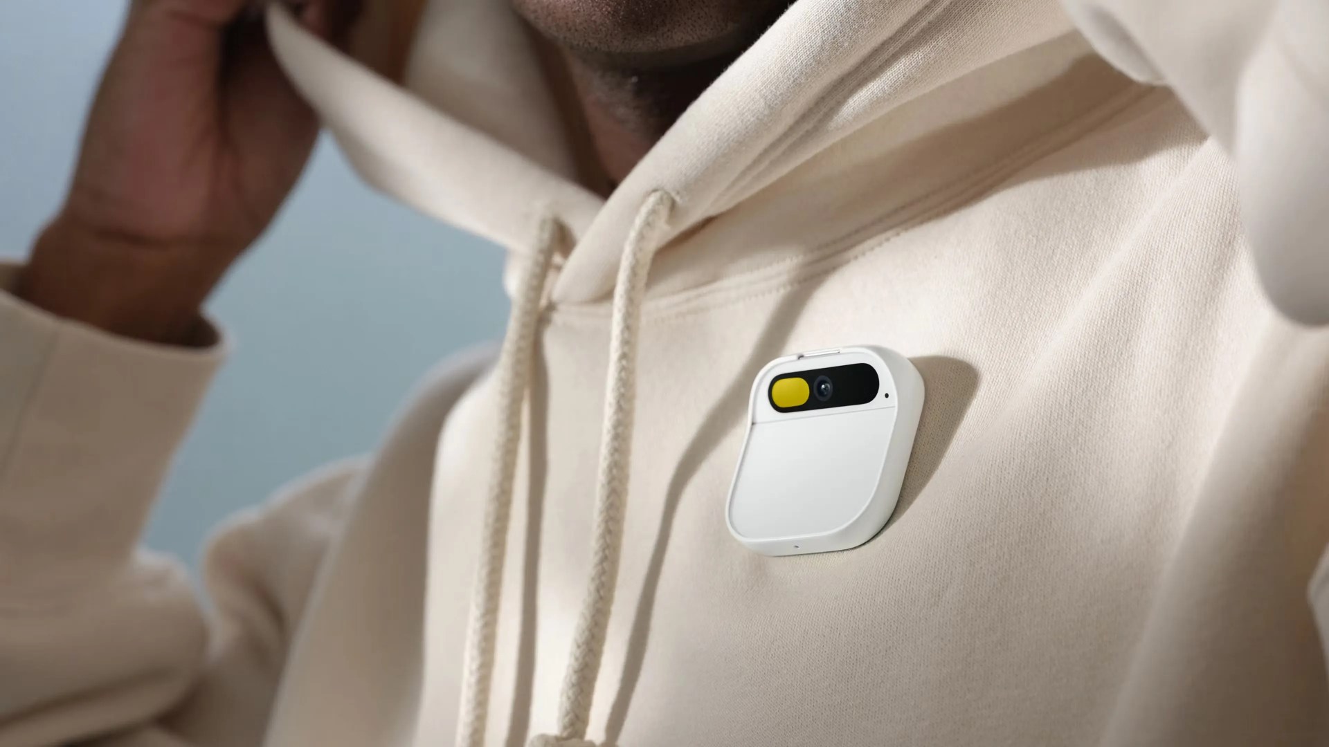 Humane AI pin in white being worn on the lapel of a person wearing a white sweatshirt.