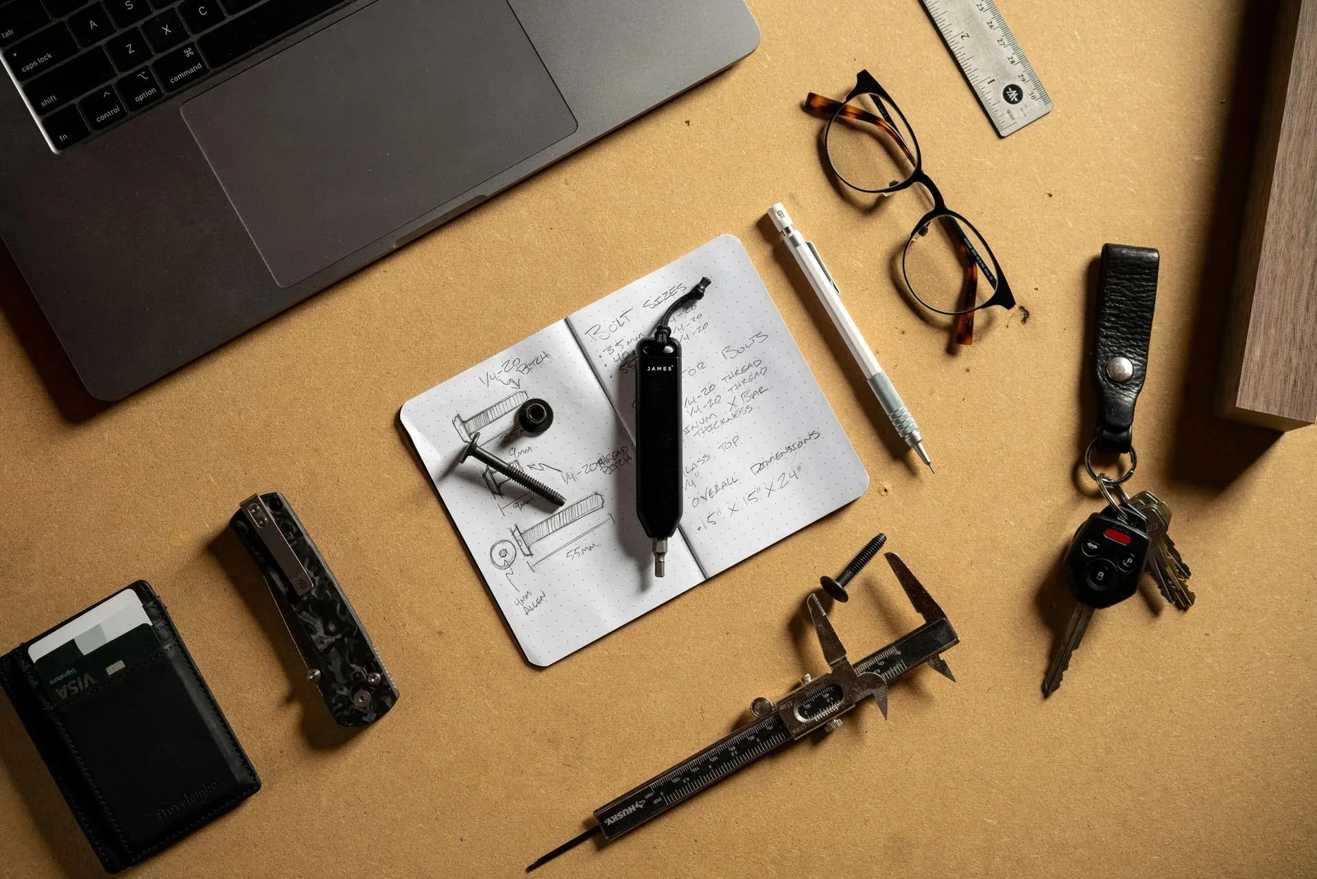 The James Brand Warrick EDC screwdriver tool sitting on table arranged alongside other every day carry items including a pencil, eye glasses and a knife.