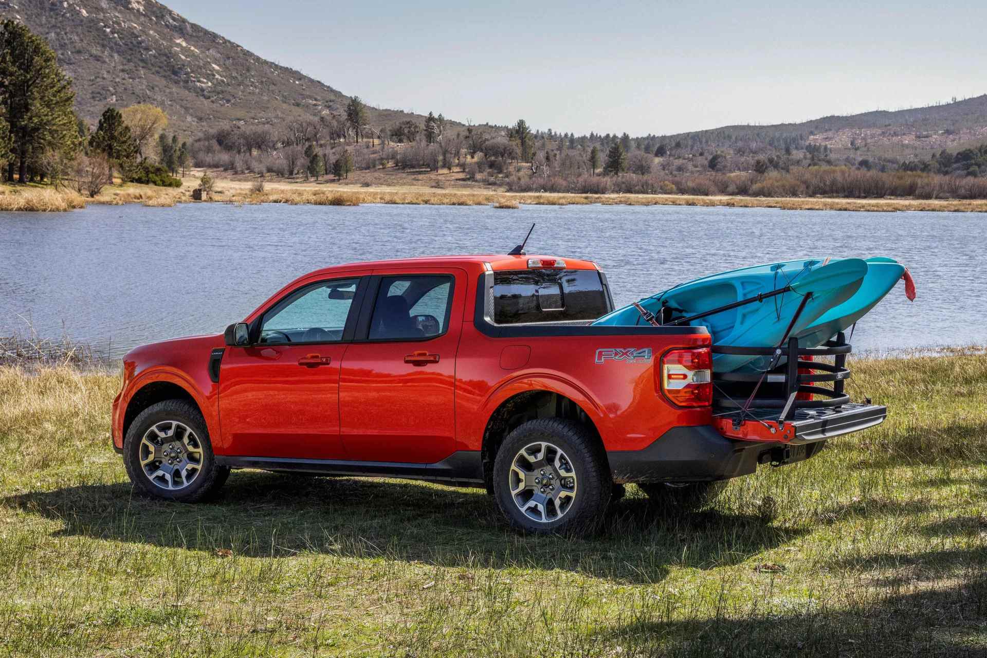 red ford maverick truck parked next to a lake with a blue kayak in the bed