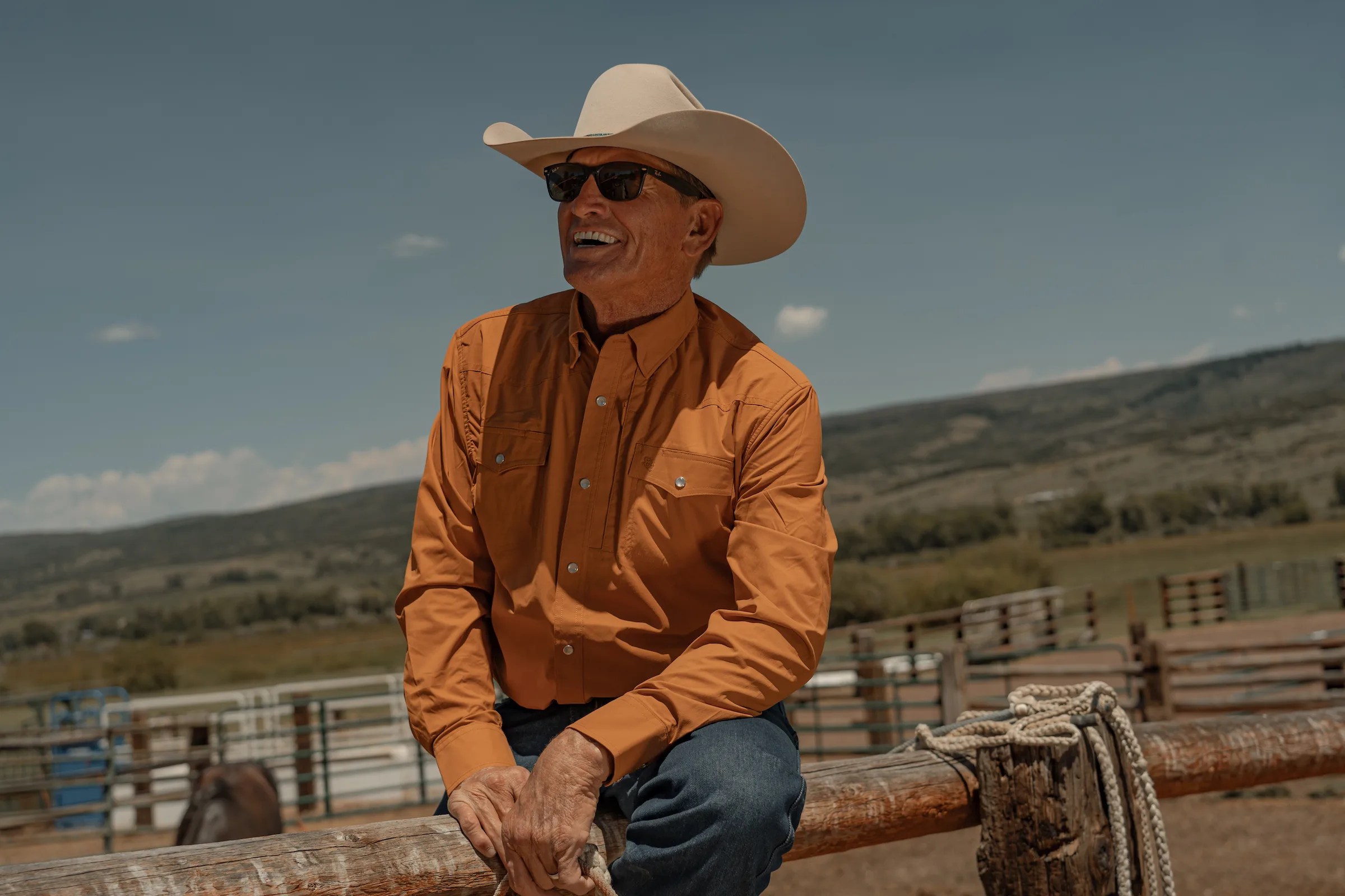 A man wears a cowboy hat and an orange Schaefer Outfitter shirt
