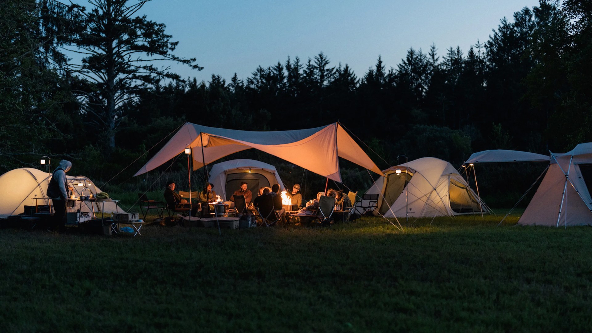 Evening scene of Snow Peak Tents and campers sitting around a campfire