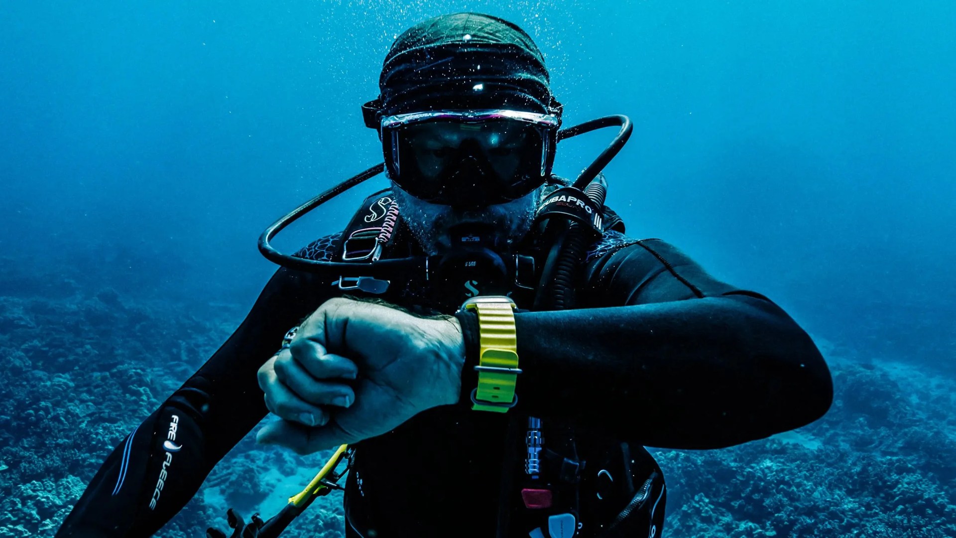 man diving underwater and looking at his yellow watch