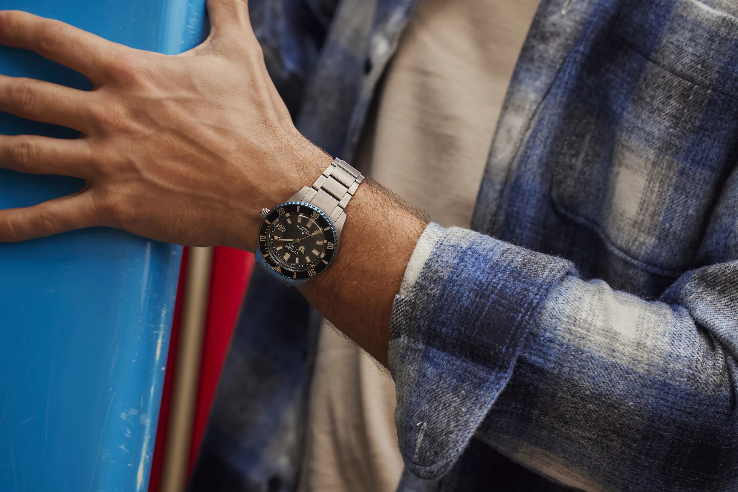 A man holds a surfboard wearing a Citizen Promaster