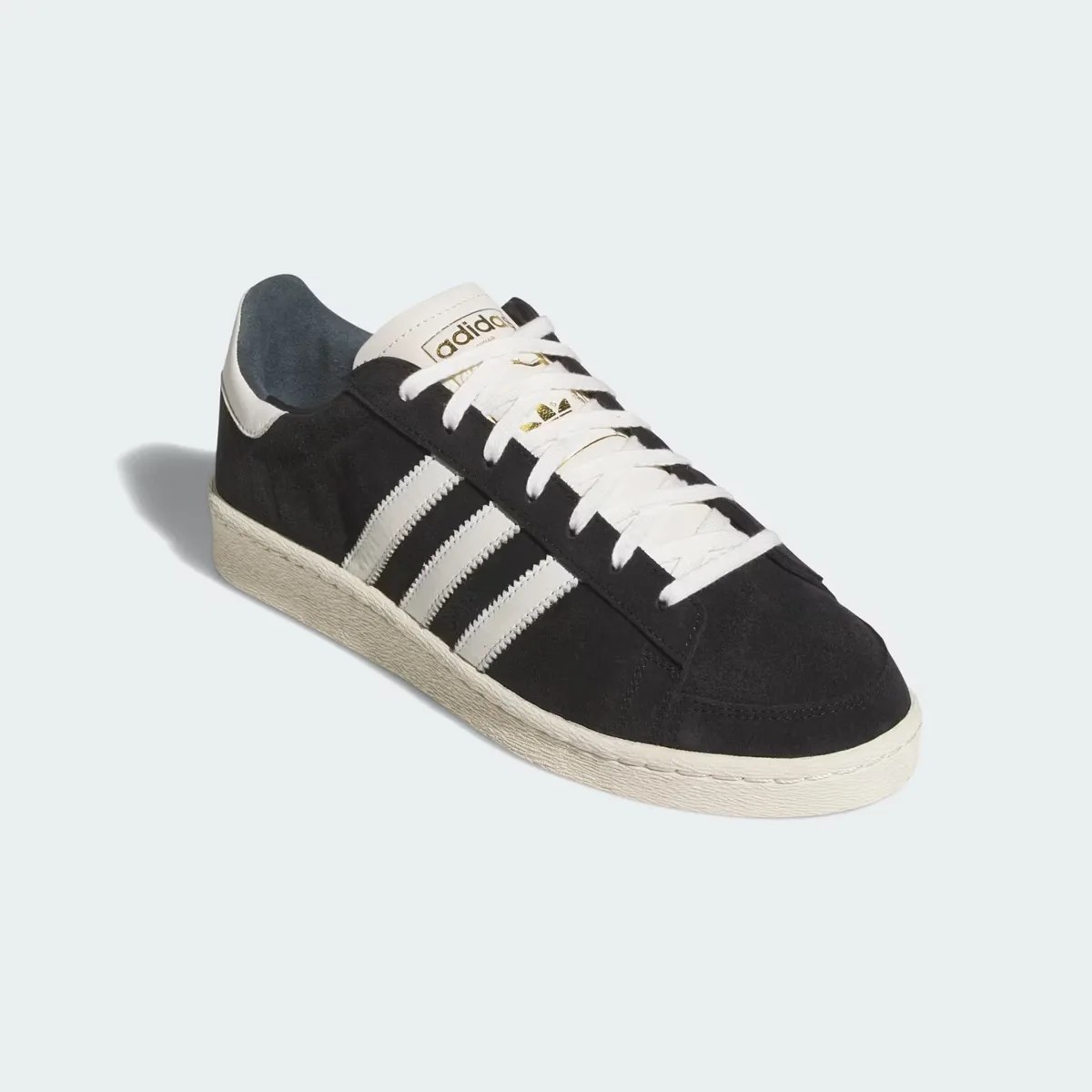 Black suede Adidas sneaker with white stripes, laces, and sole on a light background.