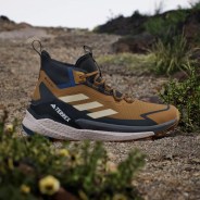 Brown and black Adidas Terrex hiking shoe with white sole and Gore-Tex label on rocky ground.