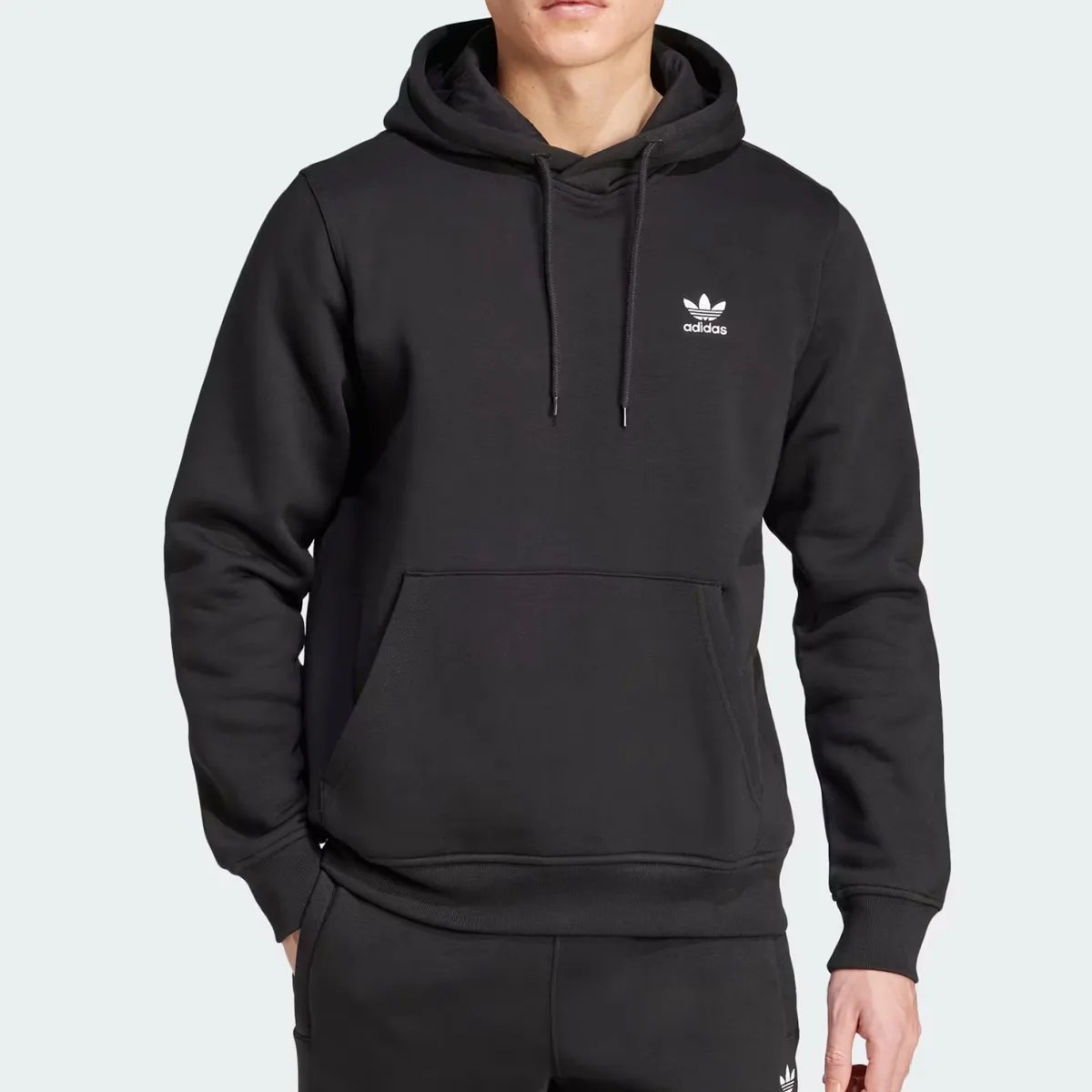 Black Adidas hoodie with front kangaroo pocket and white trefoil logo on chest worn by a person.