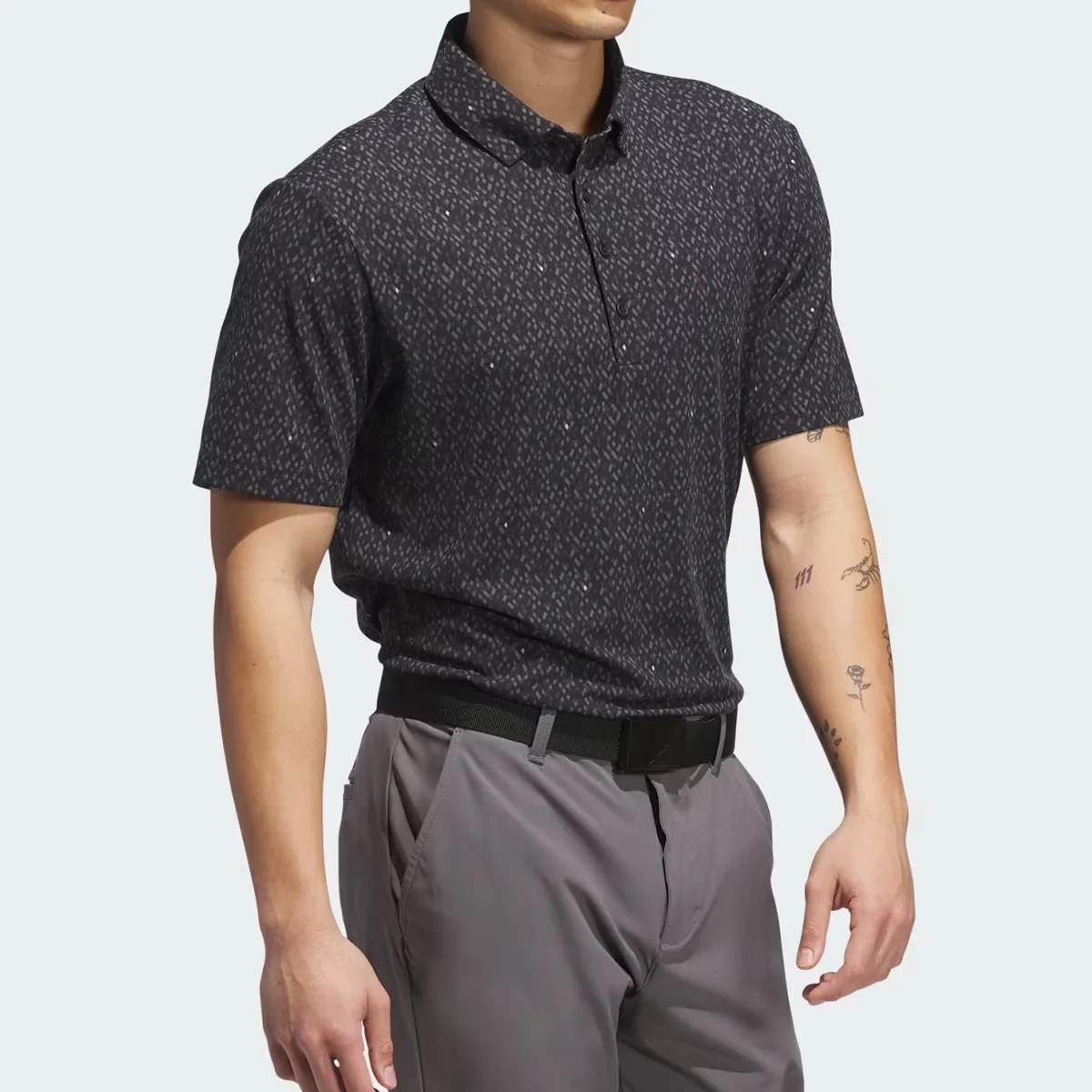Black patterned short-sleeve polo shirt worn tucked into gray pants with a black belt.