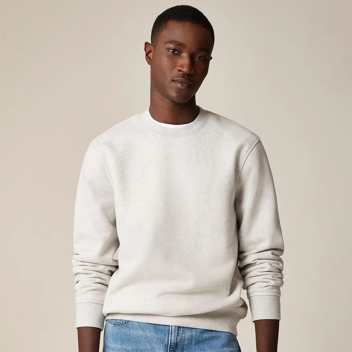 Light gray crewneck sweatshirt with long sleeves worn by a person against a beige background.