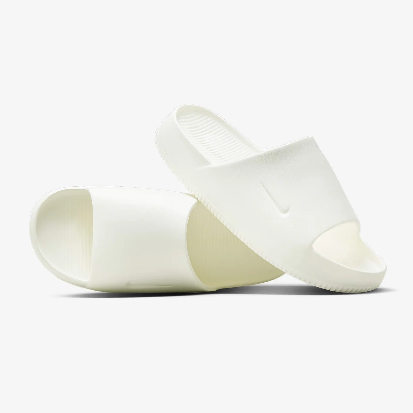 Pair of white Nike slide sandals with a wide strap featuring a subtle embossed Nike swoosh logo, textured footbed, and open toe design. The sandals have a minimalist, sleek look and a slightly elevated sole.