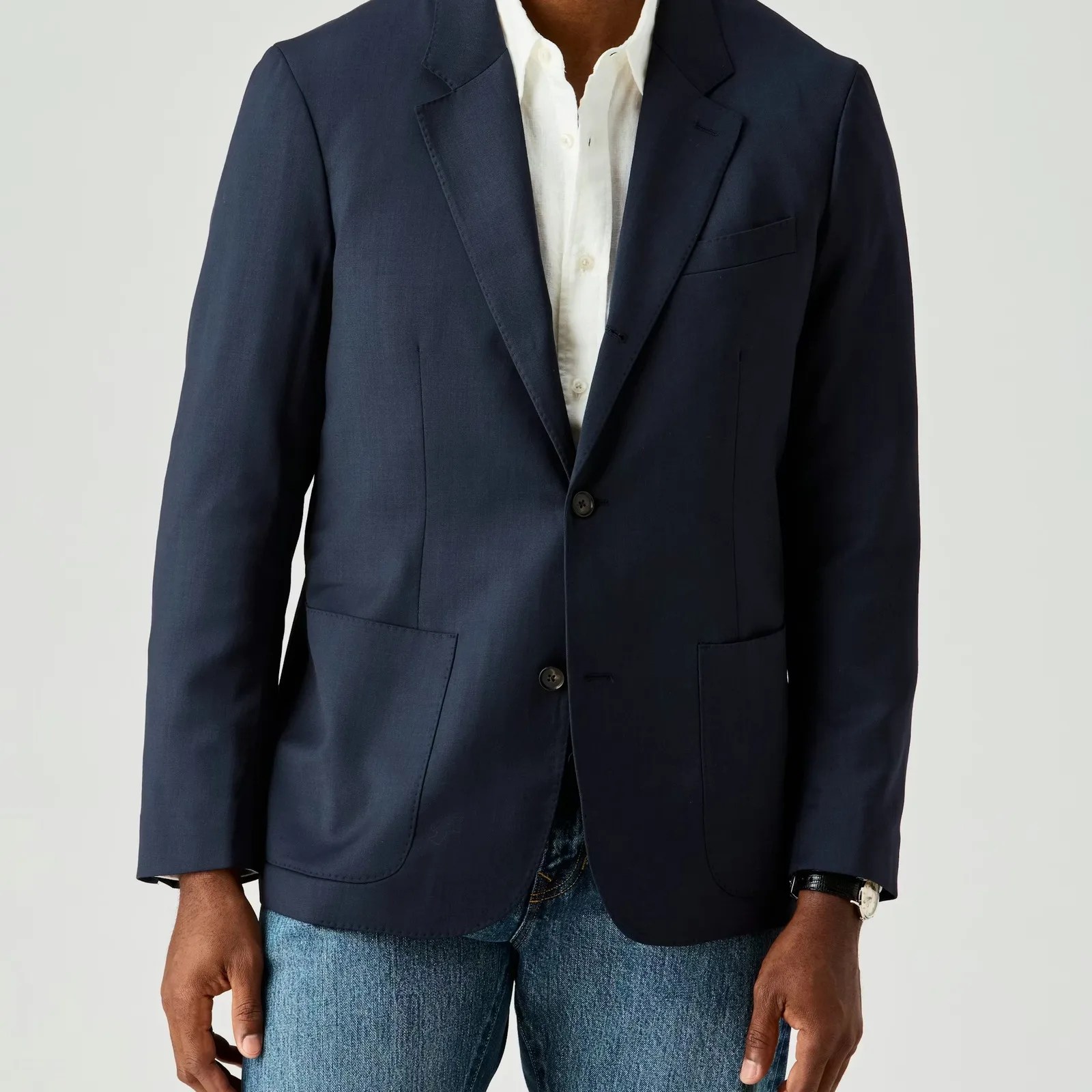 Navy blazer with notch lapels and two buttons worn over a white shirt and blue jeans.