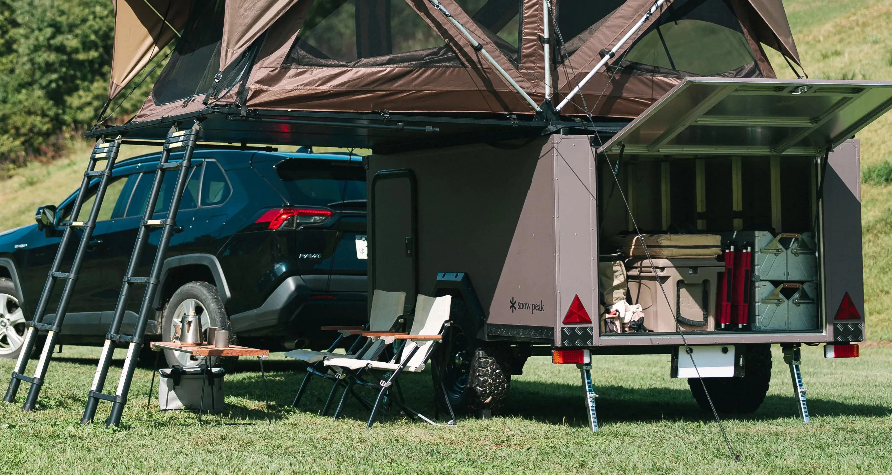 a snow peak trailer with a pop up tent sits behind a black suv