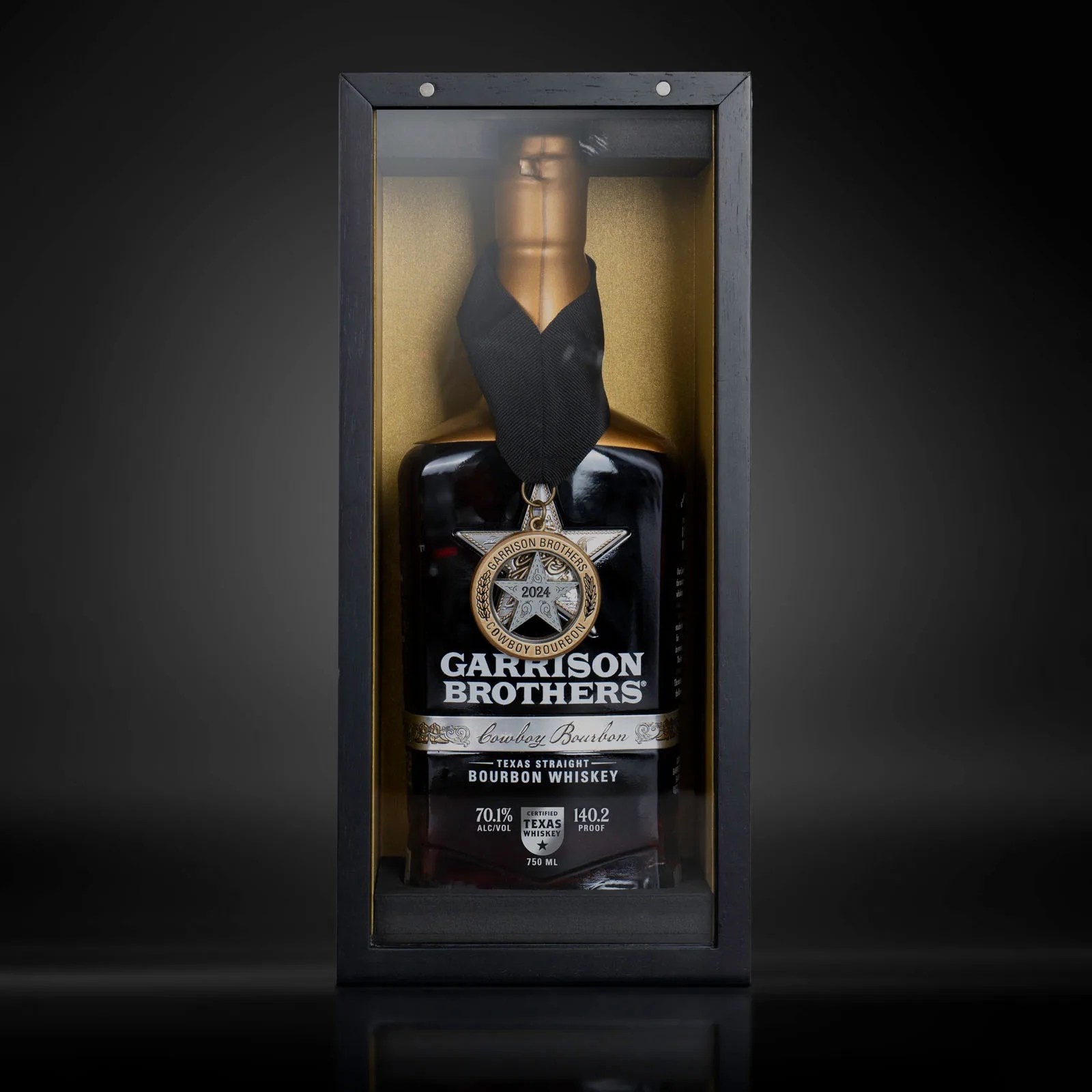 A bottle of Garrison Brothers Cowboy Bourbon 10 Year anniversary edition sitting in its special edition box against a black background.