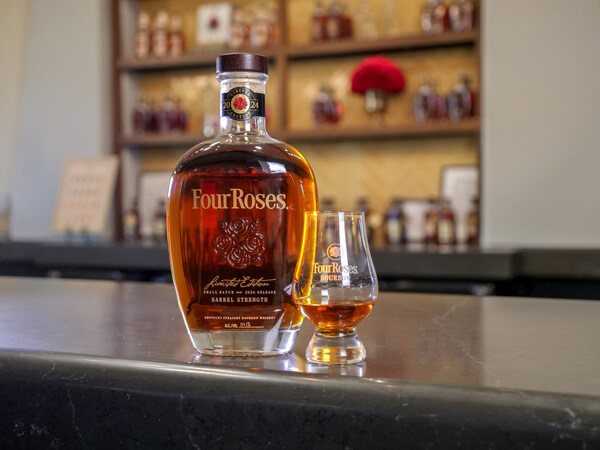 A bottle of the 2024 edition of Four Roses Limited Edition Small Batch Bourbon sitting on a bar next to a filled glencarin glass.