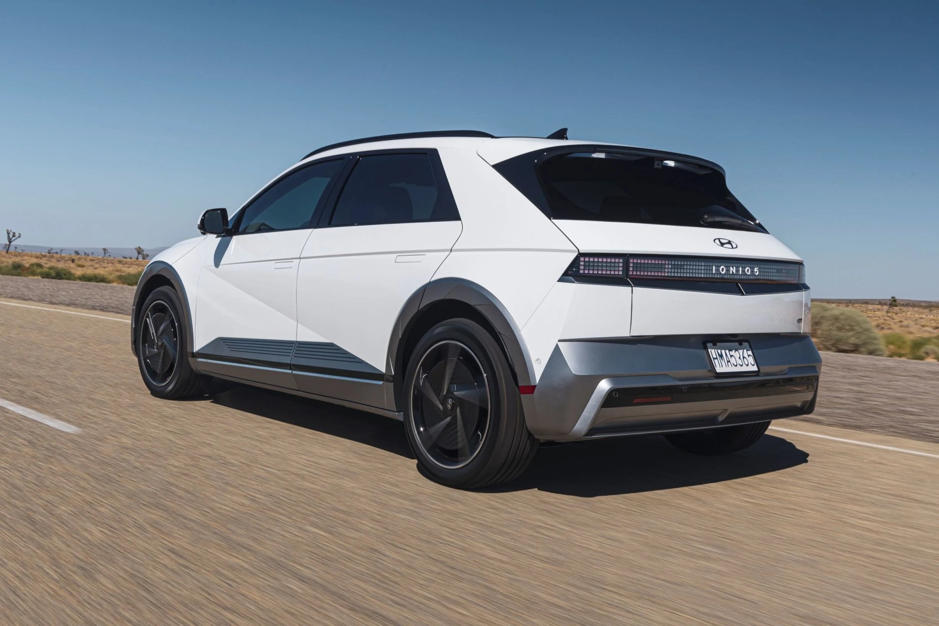 A white 2025 Hyundai Ioniq 5 driving down the road as shown from the back rear corner. 