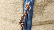A close up image of Flint and Tinder's quarter fleece jacket showing the zipper. The fleece is a cream colored