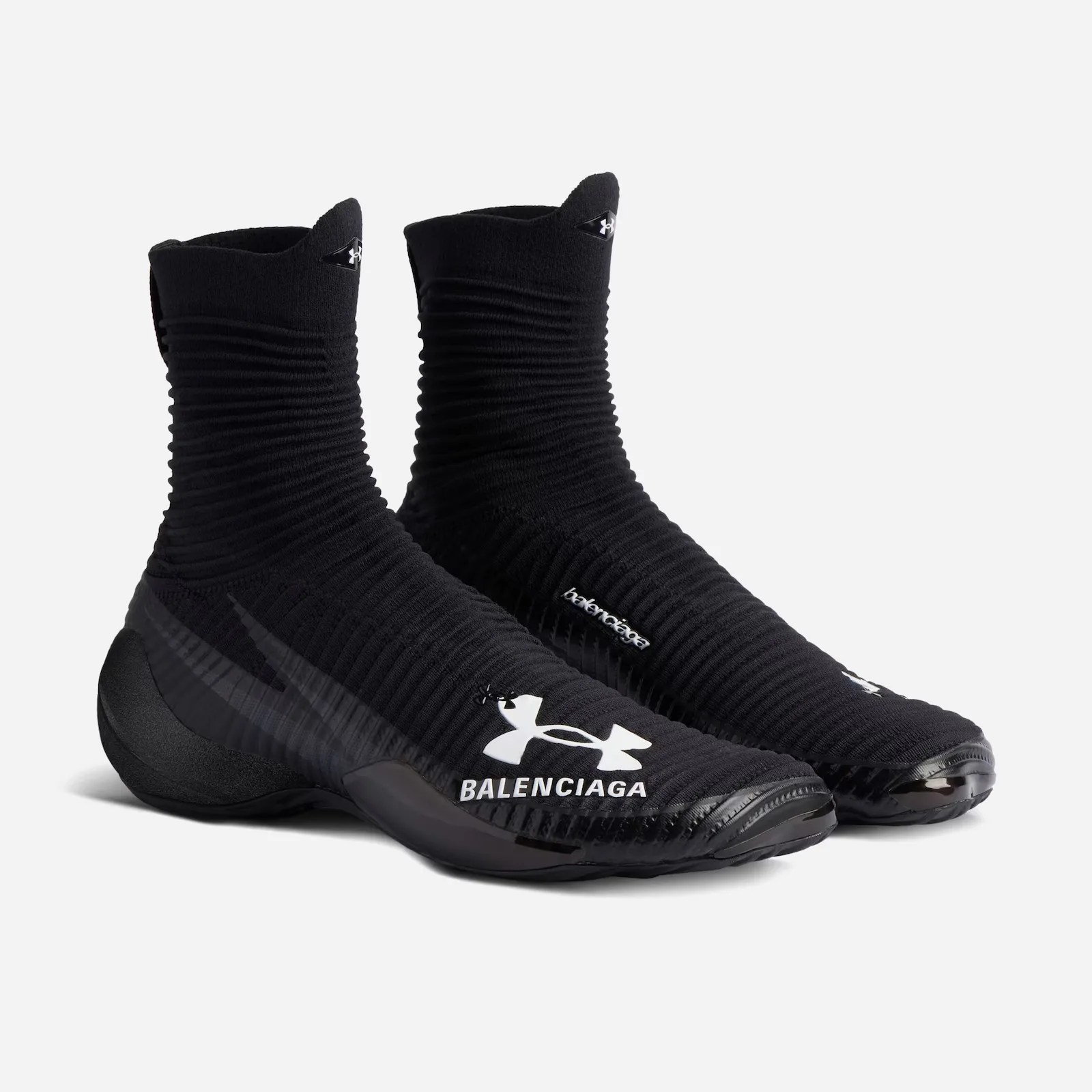 A pair of black Balenciaga x Under Armour Hyper Sneakers in black shown from an angle standing empty and side by side against a light grey background. 