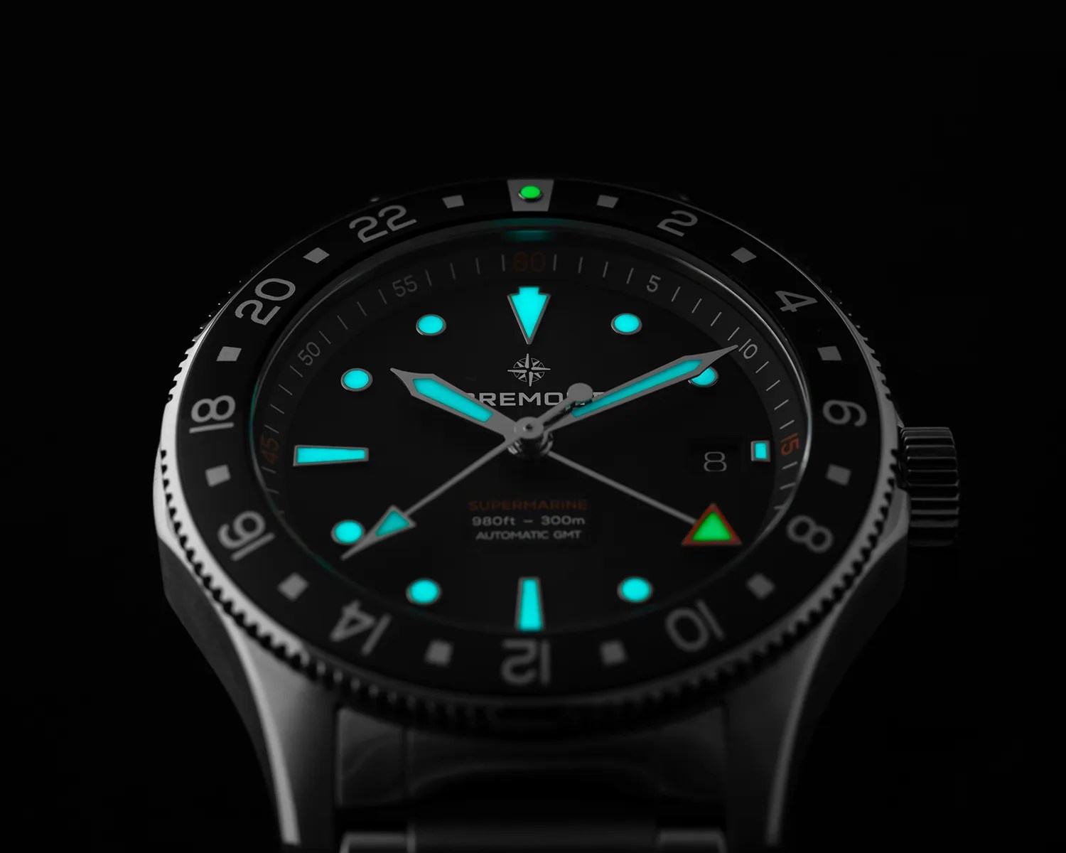 a closeup of a bremont gmt dive watch against a black background with lume glowing