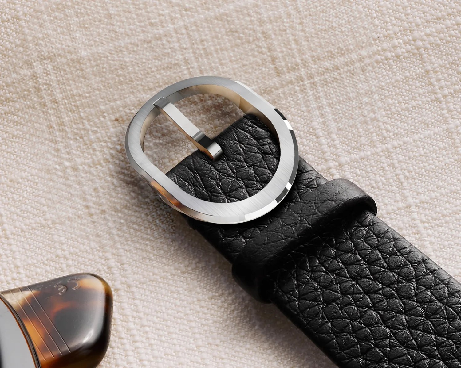 a closeup of a serica watch strap buckle against a linen background