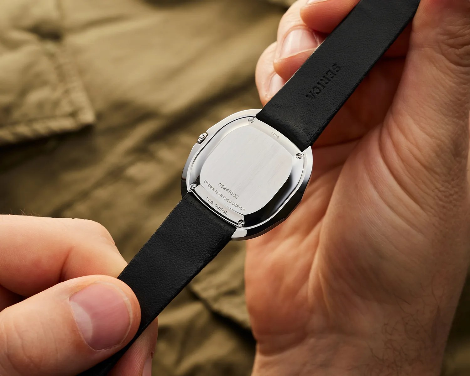 a man shows the caseback of a serica dress watch