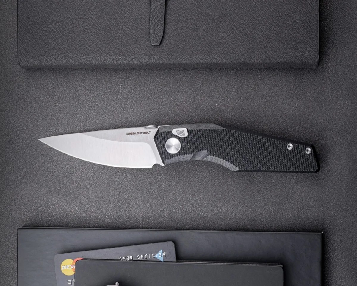 Real Steel Spectrum knife on black desktop next to notebooks and credit cards