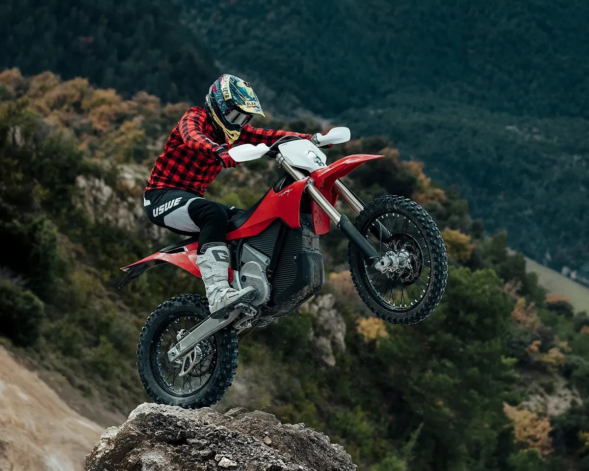 Rider pulling a wheelie on a rock aboard the Stark Varg EX in front of forest hills