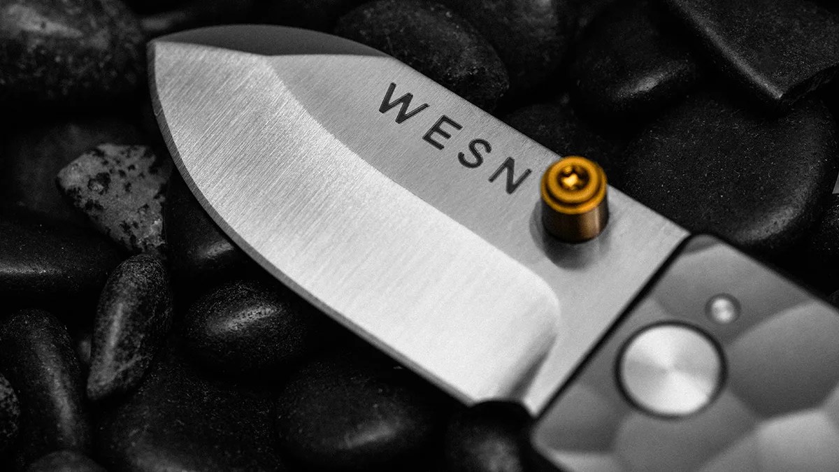 Closeup shot of WESN Ridgeback Microblade blade over black pebbles
