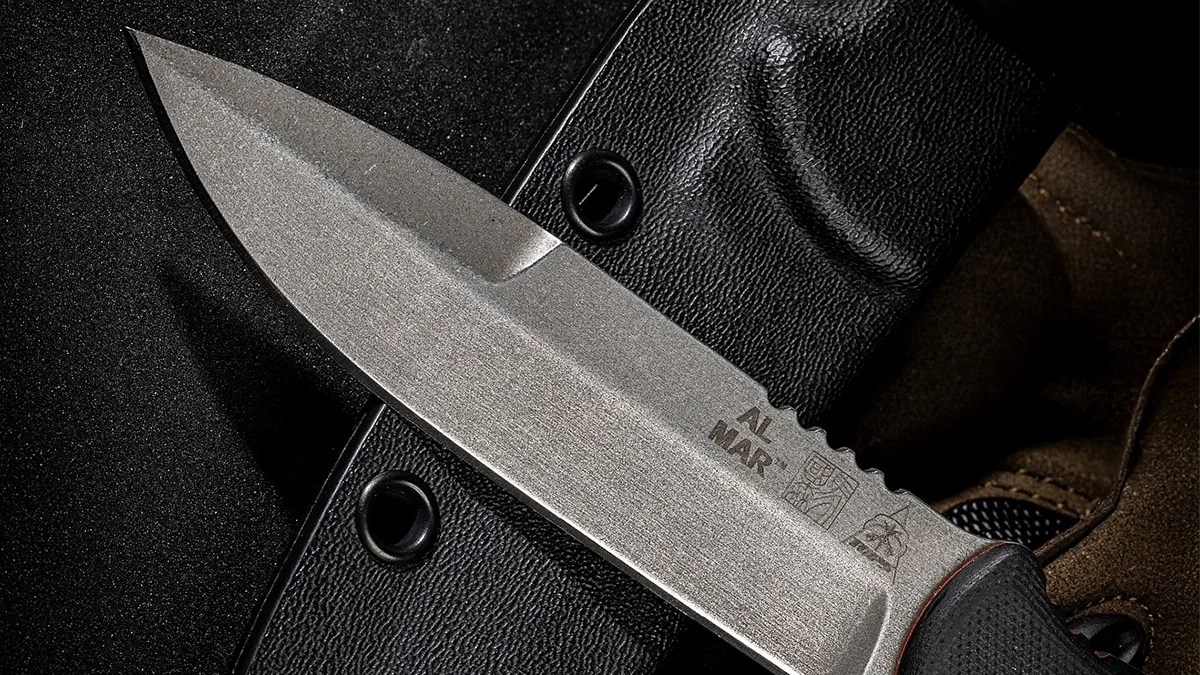 Closeup of Al Mar x Tops SERE Operator knife blade laying on tactical gloves and sheath