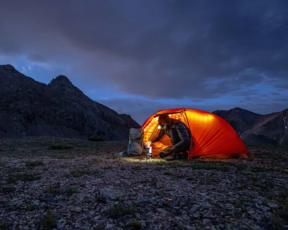 Man making a camp meal in a Big Agnes tent on a mountain