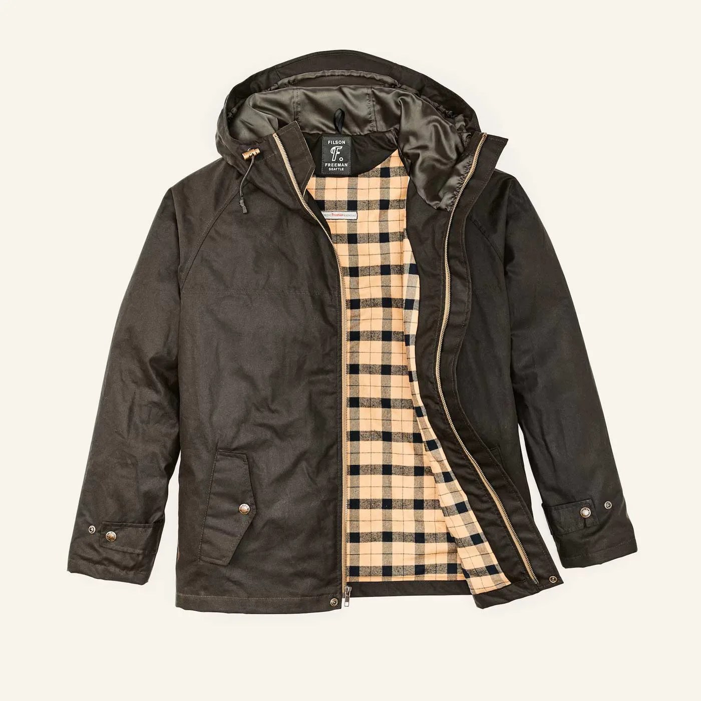 The Filson x Freeman rain jacket collaboration released in the fall of 2023. The jacket is made from a greenish brown waxed canvas and features a bright black and yellow checked flannel interior. The jacket is shown laying flat with the right side flipped slightly open to reveal the lining. 