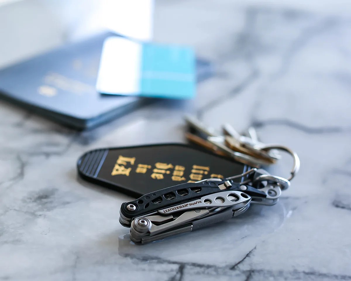 A Leatherman Style PS multitool on a keychain on a marble countertop with a passport in the background