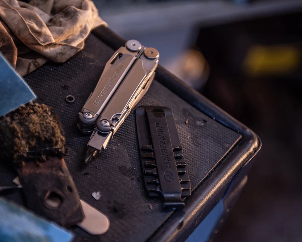 A Leatherman Wave Multi-Tool and bits on top of a workbench next to dirty rags