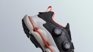 A up close shot of the heel and mid section of Merrell SpeedArc hiking shoe. The shoe is black with orange details and a white sole. The toe area of the shoe is cut off at the bottom of the image.