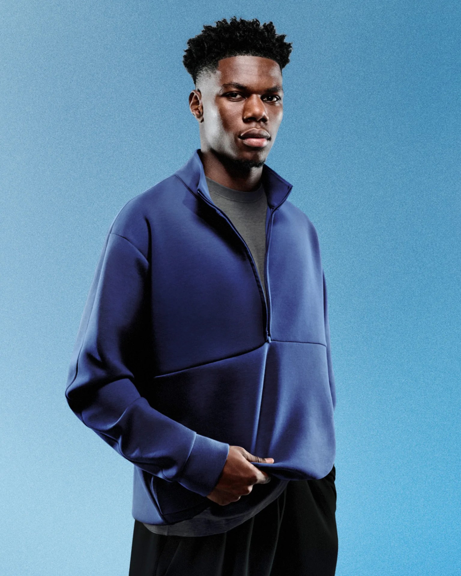 A black male model wearing a royal blue colored quarter-zip top. He model is shown looking forward but slightly turned to the side. The quarter-zip is zipped down. The background is royal blue.