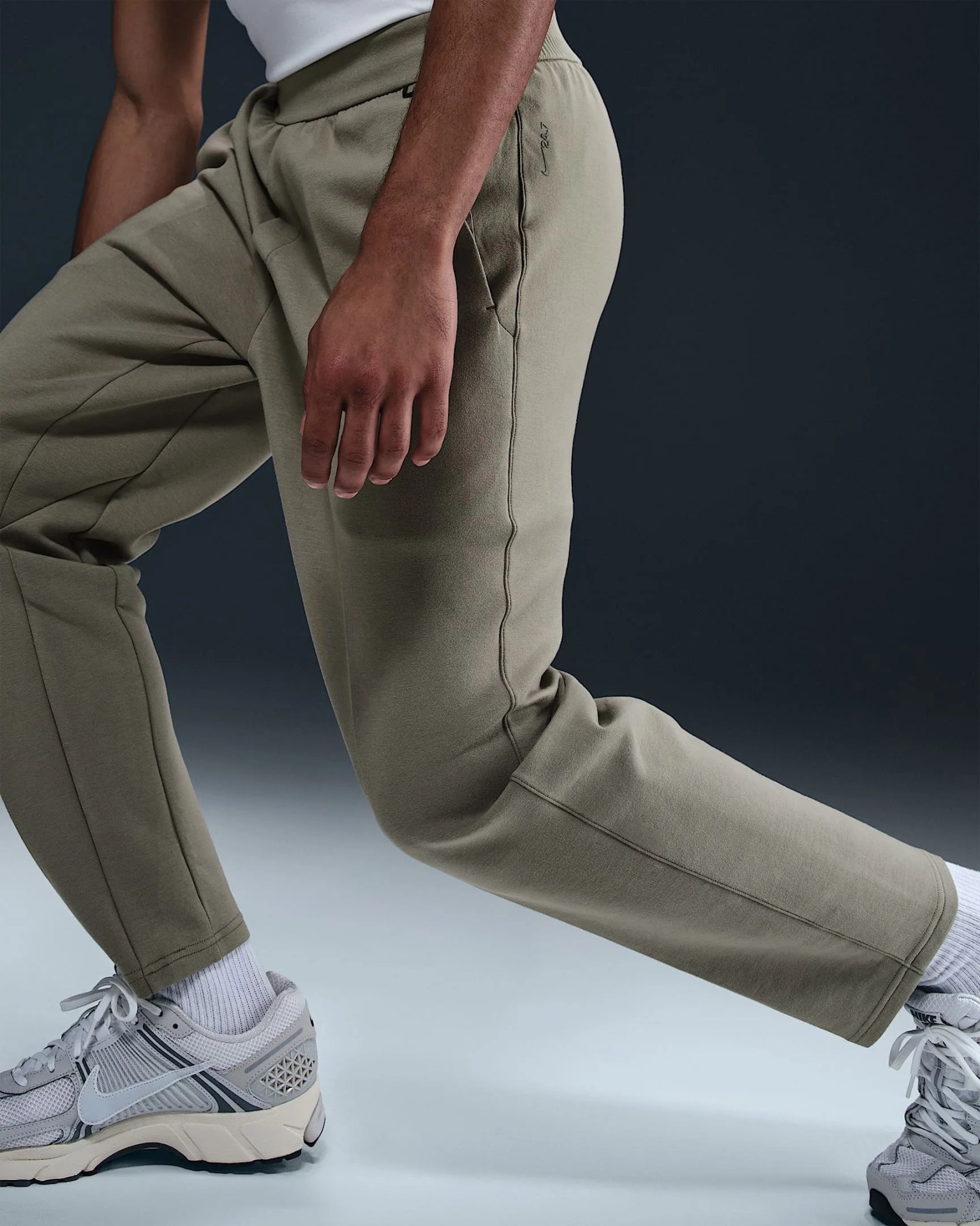 A pair of Nike 24.7 ImpossiblySoft Men's Dry-Fit pants in light tan being worn on a model whose knees are bent. 