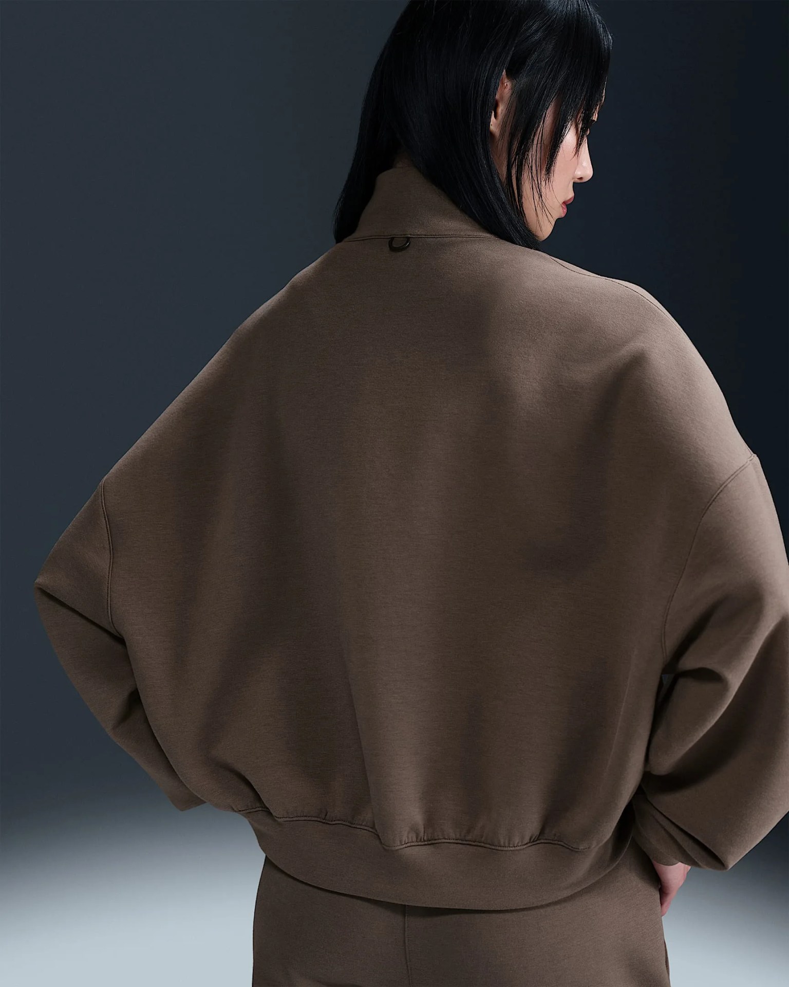A women shown from behind wearing a dark brown quarterzip with her hands on her hips. The image highlights the baggy fit of the sweatshirts. 