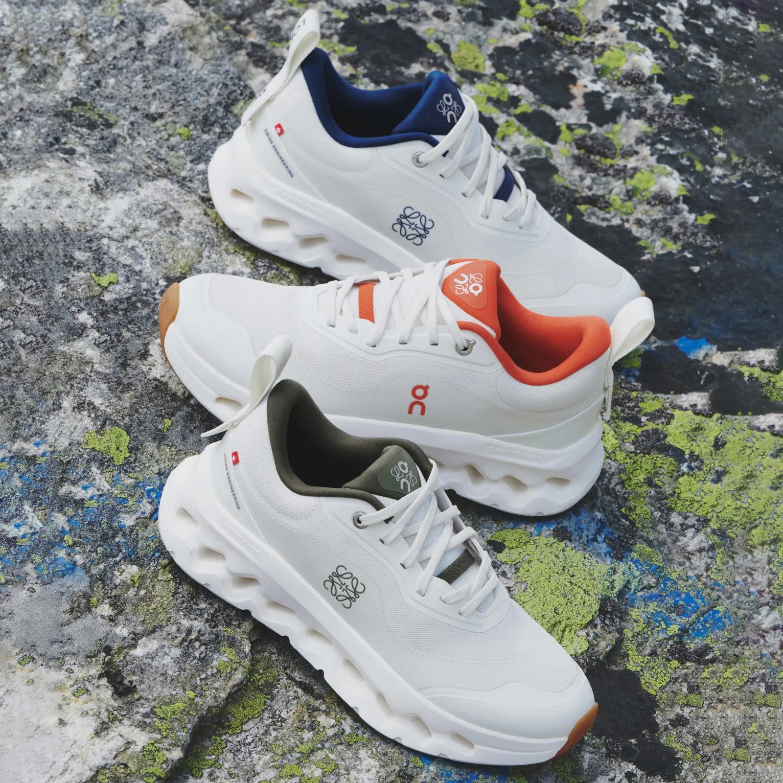 Three individual 2025 On Cloudtilt Loewe 2 running shoes in different colors shown empty and resting against a rocky surface covered with colorful moss / algae.