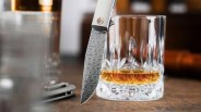 Closeup of Böker Damast Annual Knife 2025 on leather table with tin, crystal glasses and scotch bottle