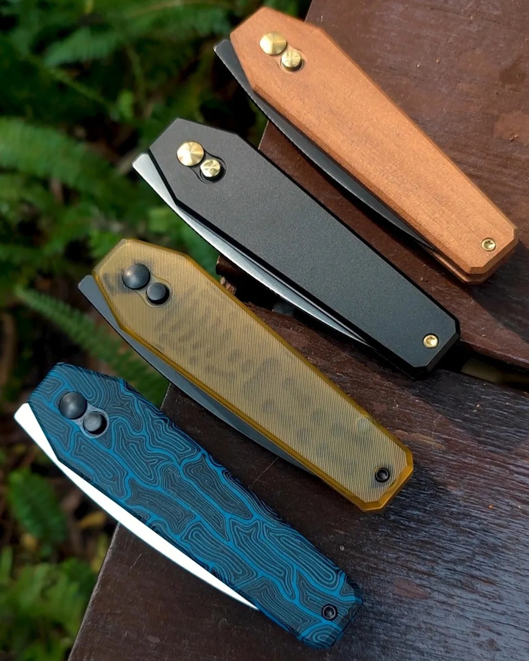 Four Kizer Tomb knife handles on outdoor bench above foliage