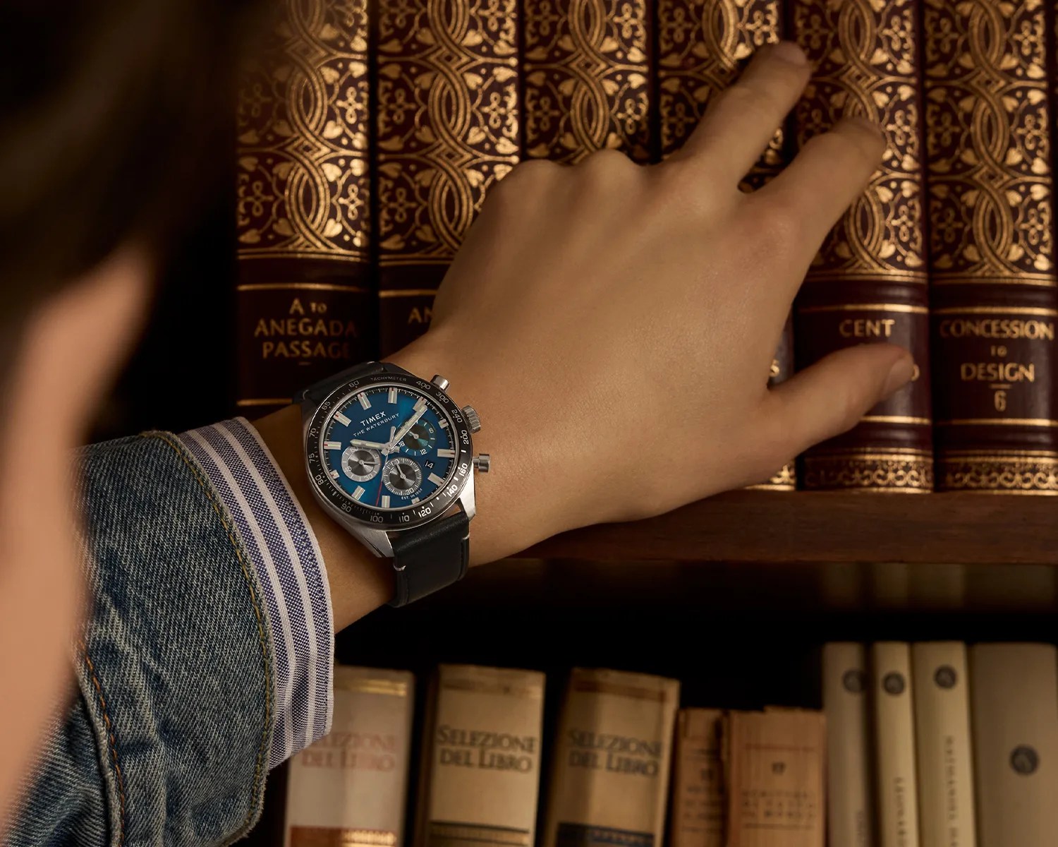 a timex chronograph watch on a mans wrist as he browses through books on a shelf