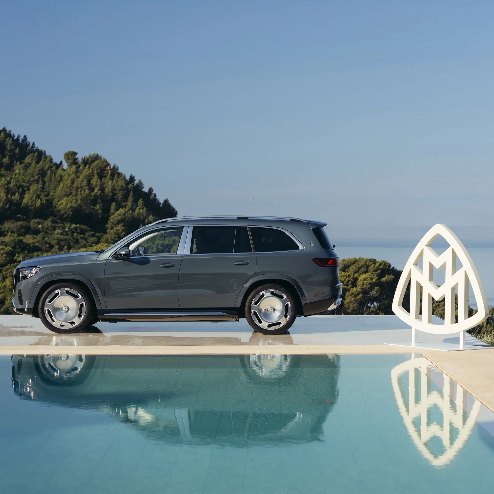 Gray luxury SUV parked beside a pool with a large white Maybach logo sculpture nearby.